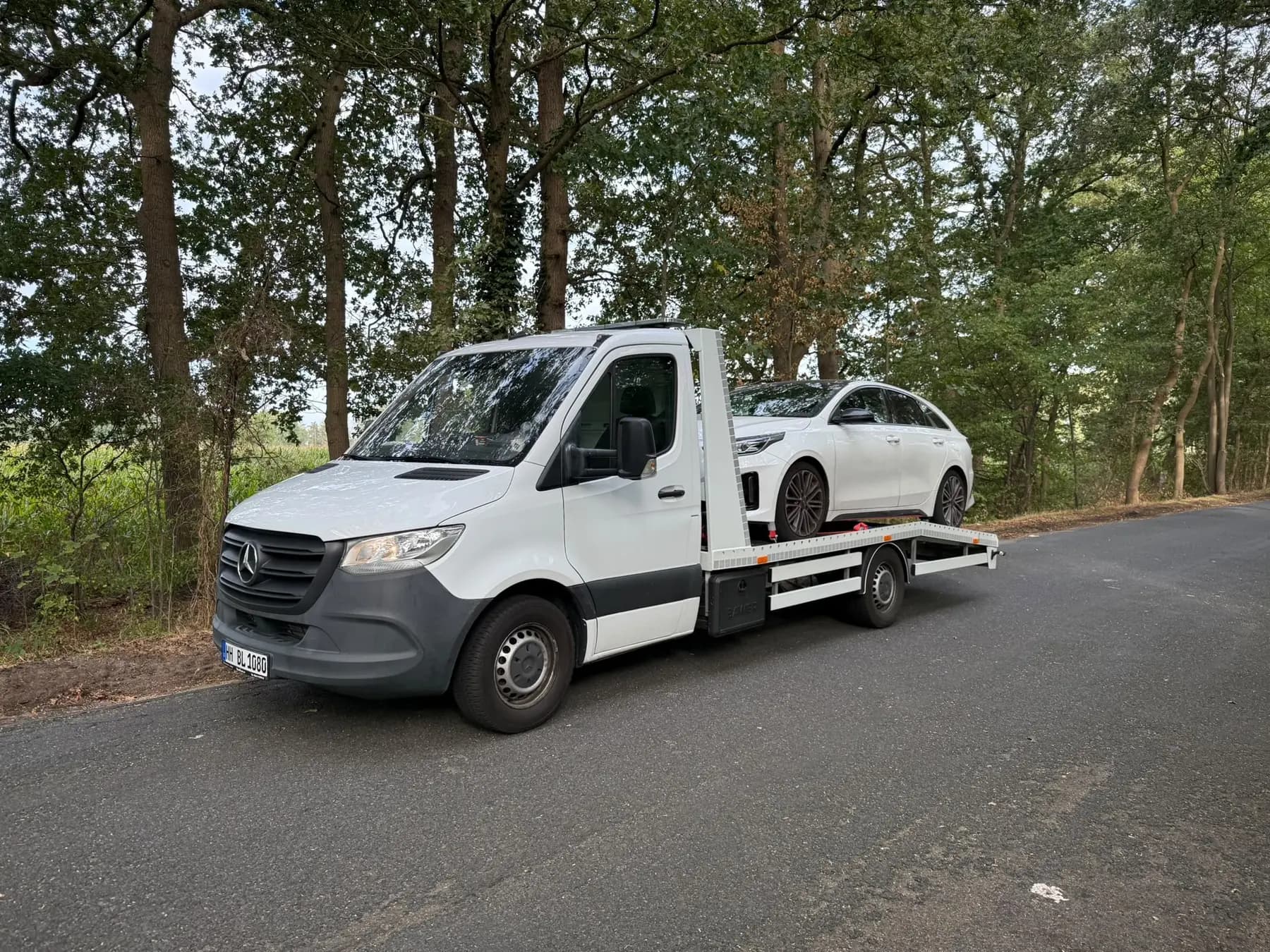 Weißer Mercedes-Abschleppwagen von BLITZ mit geladenem PKW auf einer Landstraße